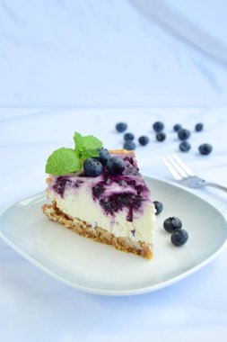 Beyaz arka planda nane yapraklı yabanmersinli cheesecake.