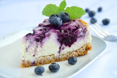 Beyaz arka planda nane yapraklı yabanmersinli cheesecake.