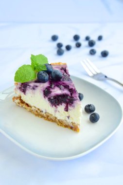 Beyaz arka planda nane yapraklı yabanmersinli cheesecake.