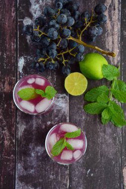 Bardakta kırmızı üzüm içeceği ve naneli buz küpleri. Arka planda üzüm meyvesi