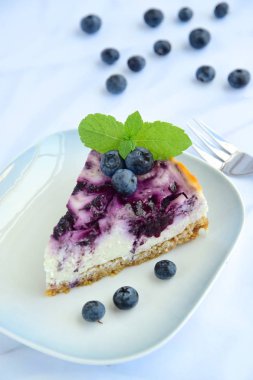 Beyaz arka planda nane yapraklı yabanmersinli cheesecake.