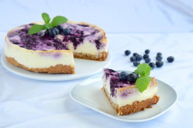 Beyaz arka planda nane yapraklı yabanmersinli cheesecake.
