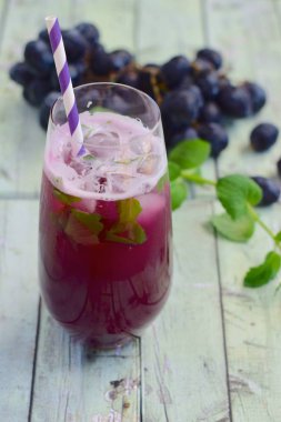 Bardakta kırmızı üzüm içeceği ve naneli buz küpleri. Arka planda üzüm meyvesi
