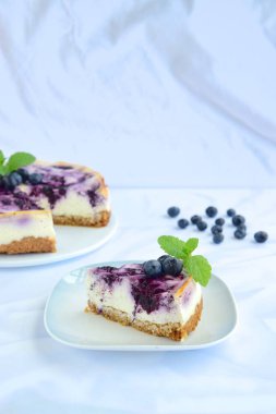 Beyaz arka planda nane yapraklı yabanmersinli cheesecake.