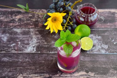 Bardakta kırmızı üzüm içeceği ve naneli buz küpleri. Arka planda üzüm meyvesi