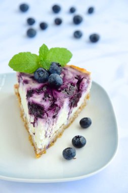 Beyaz arka planda nane yapraklı yabanmersinli cheesecake.