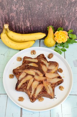 Banana pear walnut chocolate cake on serving plate, wooden background