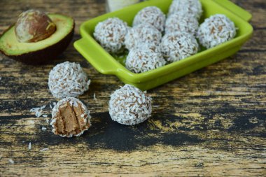 Ev yapımı çiğ avokado çikolatalı trüf, fındık, tohum ve ahşap arka planda hindistan cevizi taneleri.