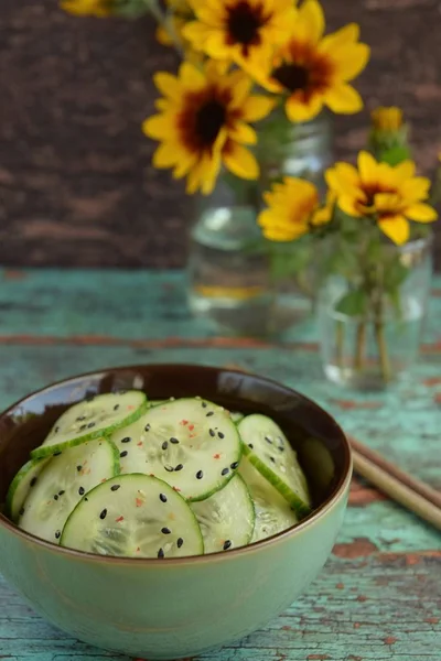Asian cucumber salad with black sesame seeds and chilli flakes. Flat lay, green wooden background, negative space.
