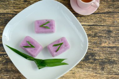 Kue Talam Ubi Ungu, geleneksel Endonezya kekleri mor tatlı patates, pirinç unu, tapyoka unu ve hindistan cevizi sütü. Beyaz tabakta servis edilen pandan yaprağıyla garnitür.
