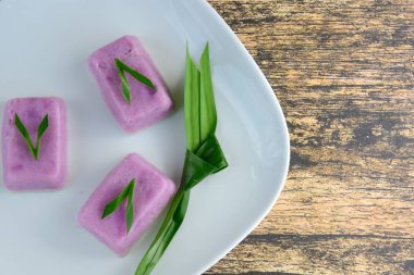 Kue Talam Ubi Ungu, geleneksel Endonezya kekleri mor tatlı patates, pirinç unu, tapyoka unu ve hindistan cevizi sütü. Beyaz tabakta servis edilen pandan yaprağıyla garnitür.