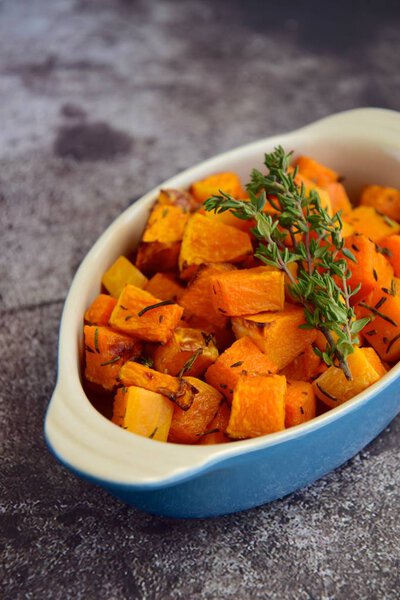 Roasted cubed butternut squash with thyme on grey background. Top view