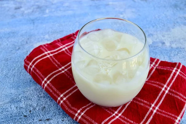 Glass of dairy free milk with ice cubes. Blue background