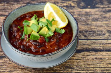 Ev yapımı vejetaryen fasulye fasulyesi çorbası, doğranmış avokado ve doğranmış maydanozla birlikte limon ile servis ediliyor.