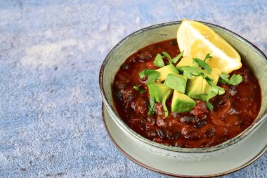 Ev yapımı vejetaryen fasulye fasulyesi çorbası, doğranmış avokado ve doğranmış maydanozla birlikte limon ile servis ediliyor.