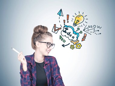 Gülümseyen bir kareli gömlek, siyah t gömlek ve bir kalem tutan ve yana doğru seyir gözlük takıyor kendine güvenen genç hipster kadın. Gri duvar arka plan iş fikir kroki ile