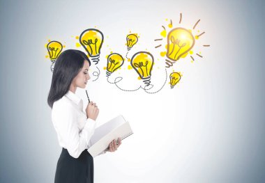 Uzun siyah saçlı beyaz bir bluz ve bir defterini tutan bir siyah etek giyen genç bir kadın yan görünüm. Gri duvar arka plan ile birçok kesimine. Bir yanar.