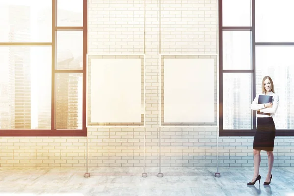 White brick wall poster gallery with loft windows with a cityscape and two vertical mock up posters hanging between them. A blonde businesswoman. 3d rendering toned image