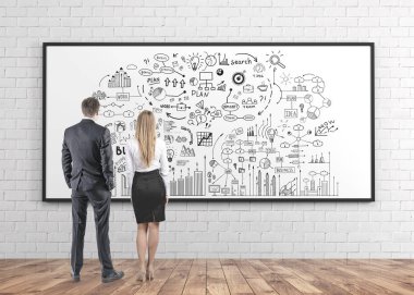 Arkadan görünüş iş ve strateji beton duvar odadaki bir beyaz tahta üzerinde çizilmiş kurmak zihin haritası bakarak takım elbise giyen genç ve başarılı iş ortakları.