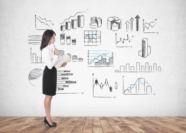 Uzun siyah saçlı beyaz bir bluz ve bir defterini tutan bir siyah etek giyen genç bir kadın yan görünüm. Bir beton duvara grafikler farklı türleri. Veri temsil ve borsa kavramı