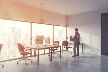 Afrika kökenli Amerikalı işadamı beyaz ve cam duvarlar, beton zemin ve şehir manzaralı bir penceresi boyunca ayakta birkaç bilgisayar masaları ile panoramik bir ofiste. 3D render sahte tonlu görüntü
