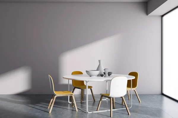 White wall minimalistic Scandinavian style dining room interior with a concrete floor, a round table and four yellow chairs. A mock up wall. 3d rendering