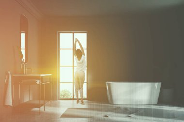 Bir gri duvar çatı banyo iç bir beton zemin ile germe kadın. Açısal bir beyaz küvet pencerenin duruyor. Bir ayna ile bir lavabo. 3D render sahte kadar çift tonlu görüntü pozlaması