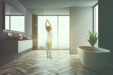 Gri banyo iç ahşap zemin, çatı windows ile bir saksı bitki yanında beyaz bir küvet. Çift lavabo ve bir kadın. 3D render sahte kadar çift tonlu görüntü pozlaması