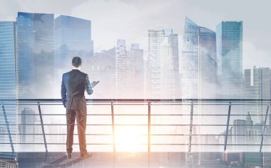 Dikiz gri elbiseli bir klasör tutan genç bir işadamı. O iple çekiyor. Sabah cityscape arka plan. Gökdelen balkonludur. Tonlu görüntü pozlama sahte katlayın