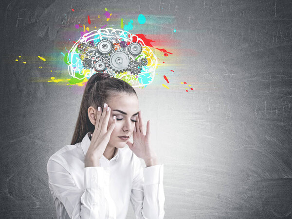 Stressed young businesswoman with long hair in a ponytail wearing a white shirt. She is having a headache. A blackboard background with a cog brain sketch on it. Mock up