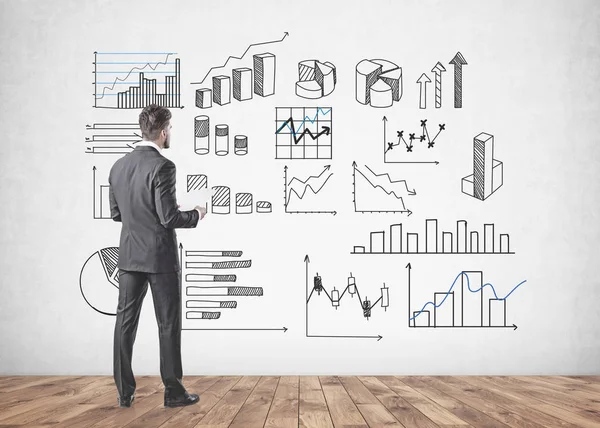 Gri takım elbise giymiş bir sakallı genç işadamı duran ve kağıtları tutarak. O iple çekiyor. Bir beton duvara grafikler farklı türleri. Veri temsil ve borsa kavramı