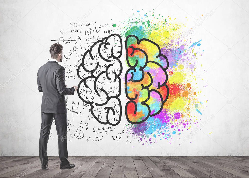 Young businessman with a beard wearing a gray suit is standing and holding papers. He is looking forward. A concrete wall with a colorful brain sketch