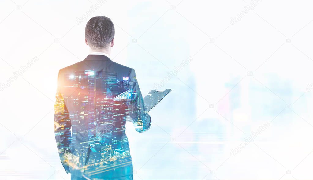 Rear view of a young businessman in a gray suit holding a folder. He is looking forward. Night cityscape background. Toned image double exposure mock up