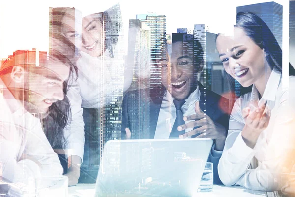 Members of a diverse business team sitting together at a table with a laptop. A cityscape background. Concept of start up success. Toned image double exposure mock up.