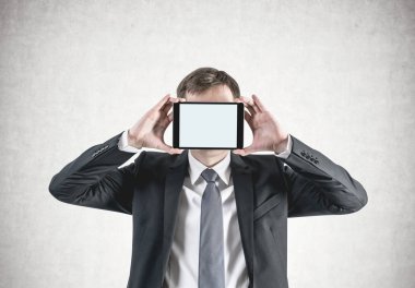 Tanınmayan bir genç beyaz işadamı portresi ile boş bir tablet ile kopya alanı yüzünü önünde tutan sarı saçlar kırpılmış. Kadar alay et. Beton duvar arka plan