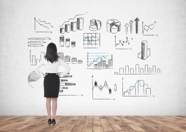 Bel ellerde ile ayakta ve ileriye dönük uzun siyah saçlı Genç bir iş kadını arkadan görünüş. Bir beton duvara grafikler farklı türleri. Veri temsil ve borsa kavramı