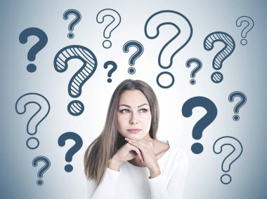 Baş ve omuz portre sarı saçlar beyaz ve yana doğru düşünme seyir ile güzel bir genç kadın. Birçok soru işareti gri bir duvar.