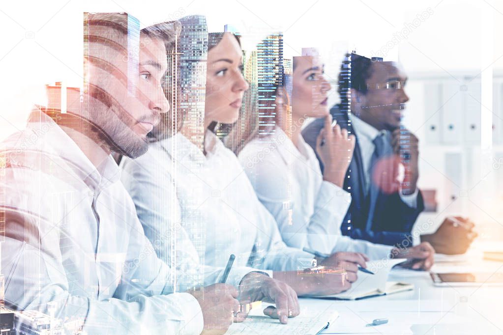 Members of a diverse business team sitting together at a table looking forward. A cityscape background. Concept of HR success and job interview. Toned image double exposure mock up.