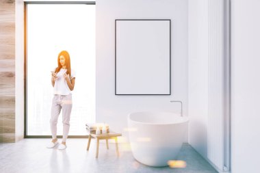 Beyaz banyo iç bir beton zemin, çatı penceresi ve beyaz bir küvet. Duvardaki poster çerçevesi kadar dikey sahte. Kadın bir telefon 3d render ile görüntü tonda