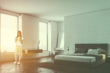 Beyaz duvarları, ahşap zemin ve king size Yataklı lüks yatak köşesinde bir cep telefonu olan kadın. İskandinav tarzı. 3D render sahte kadar çift tonlu görüntü pozlaması