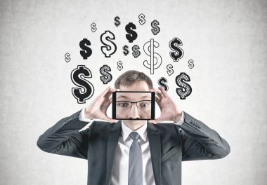 Sarı saçlar onun yüzüne zoom ile bir tablet holding ile yakışıklı bir genç beyaz işadamı portresi kırpılmış. Beton duvar arka plan üstünde dolar işareti ile