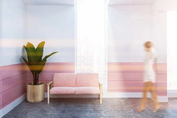 Woman in the lobby of a white and pink spa with a concrete floor, a pink sofa and a potted plant in the corner. 3d rendering mock up toned image blurred