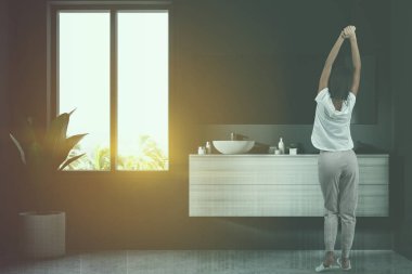 Kadının yanına Beyaz ahşap tezgah üzerinde duran çift banyo lavabo. Bir ayna üzerinde gri bir duvarda asılı duruyor. Köşedeki saksılı bir bitki. Şehir 3d render kadar alay tonda görüntü çift pozlama