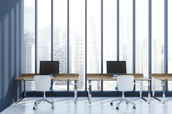 Open space office interior with dark blue walls, a concrete floor, rows of wooden computer desks and white chairs. Panoramic window with a cityscape. 3d rendering mock up
