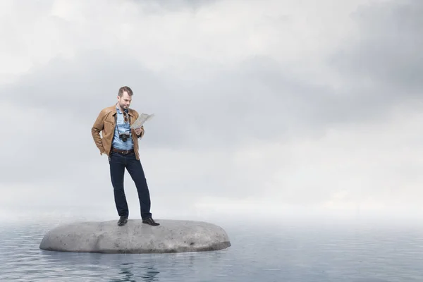 Lost young tourist man looking at a map standing on a flat rock in open sea. Cloudy sky. Concept of losing your way in business and life. Challenging problem solving. 3d rendering mock up