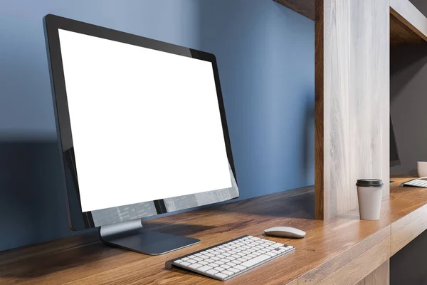 Blank computer screen standing on a wooden table in an office interior situated in a blue wall room. Side view. 3d rendering mock up
