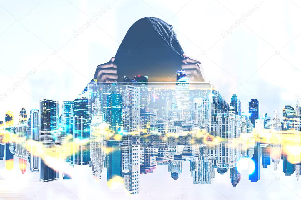 Unrecognizable young hacker in a black hoodie sitting near his laptop. A night city foreground. Concept of cyber security. Toned image double exposure