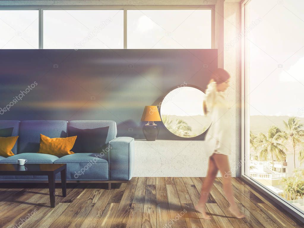 Woman walking in a blue living room interior with a wooden floor, a blue sofa and a round mirror on the closet. 3d rendering toned image