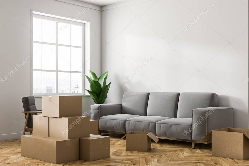 Empty white room corner with white walls, a wooden floor, a large window and stacks of closed cardboard boxes. A gray sofa. Concept of moving in. 3d rendering mock up