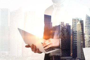 Tanınmayan işadamı gökdelenler ile sabah şehir arka plan üzerinde bir laptop ayakta tutan. Tonlu görüntü pozlama sahte katlayın